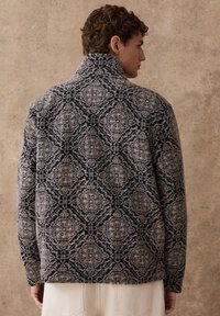 Toppis, millel on kõrge krae, millel on tumesinine ja hall keerukas lillemuster. Pehme tekstuur ja lõdvestunud lõige, sobib kihitamiseks.