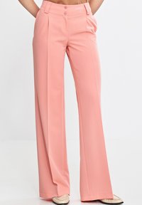 Spodnie o szerokich nogawkach w miękkim różowym materiale, z wysokim stanem i dwoma guzikami, z plisami oraz gładką fakturą. Casualowy fason.