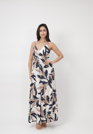 Kvinde iført ærmeløs V-hals maxi-kjole med pink, navy og hvidt bladmønster, stående med hånden på hoften mod en hvid baggrund.