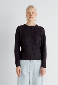 Maglione grigio scuro a maglia con scollo rotondo e orlo a costine. Presenta maniche lunghe e una vestibilità morbida. Indossato con pantaloni larghi azzurri.