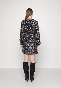 Robe à motifs noir et blanc avec manches longues, taille cintrée et jupe évasée, associée à des bottes noires montantes ornées de clous.