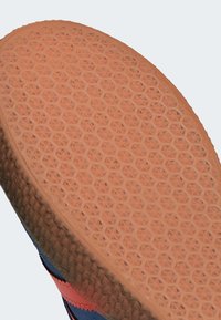 Suela de zapato con patrón de tacos hexagonales en goma marrón claro sobre un zapato azul y rojo.