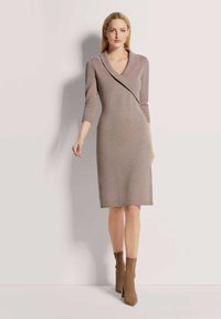 Strickkleid in Mauve mit V-Ausschnitt, dreiviertelÄrmeln und taillierter Silhouette. Eine glatte Textur und Stiefeletten ergänzen den Look.