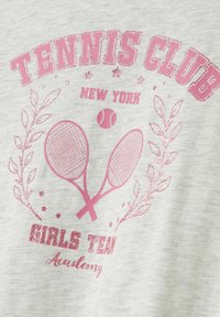 Camiseta de tela gris con un diseño gráfico en color rosa que presenta raquetas de tenis cruzadas, una pelota de tenis y el texto "Tennis Club New York Girls Team Academy."