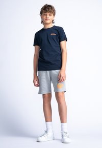 T-shirt en coton bleu marine avec un petit graphisme, associée à un short gris arborant un logo orange, et des baskets blanches avec des chaussettes de cheville.
