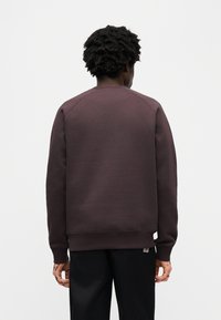 Σκούρο μοβ φούτερ με στρογγυλή λαιμόκοψη και ριμπ μανσέτες. Διαθέτει ραφή στην πλάτη χωρίς ραφές και υφή υφάσματος. Φοριέται με μαύρο παντελόνι.