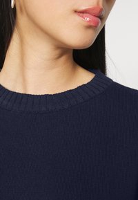 Maglione in maglia a costine blu navy con un ampio scollo a giro, caratterizzato da un motivo testurizzato lungo il collo e una finitura liscia sulla stoffa.