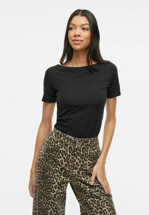 T-shirt noir à manches courtes avec un col rond, associé à un pantalon large beige à imprimé léopard, avec une taille visible et des poches.