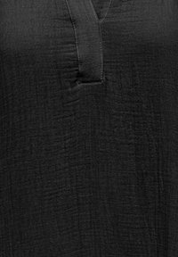 Tela negra texturizada con tapeta en forma de V en la parte delantera y detalles de costura visibles.