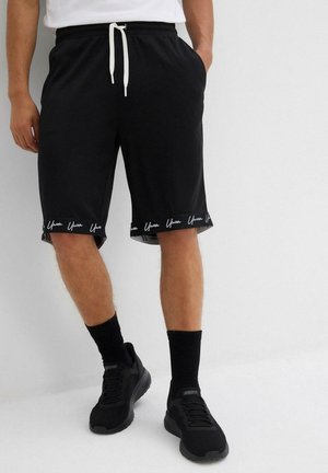 Shorts de sport noirs en tissu léger, avec une taille élastique munie d'un cordon de serrage et un logo contrasté à l'ourlet.