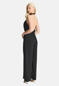 Zwarte jumpsuit met een halternek versierd met pailletten en een open rug, met wijde broekspijpen en een subtiele glans. Strappy hakken maken de look compleet.