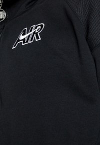 Svart sweatshirt med texturerade axelpaneler. Har en vit "AIR"-logotyp och dragkedja i halsen. Tyget är mjukt med en slät finish.
