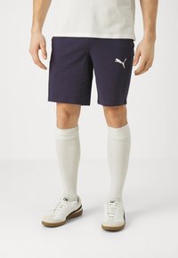 Námořnické sportovní šortky s vyšívaným bílým logem Puma, doplněné bílými ponožkami po kolena a bílými teniskami s béžovými akcenty.