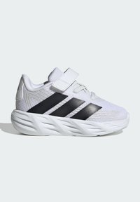 Chaussure de sport blanche avec des rayures noires, tige en mesh, semelle épaisse et rembourrée, lacets et une bride Velcro sur le dessus pour un maintien sûr.