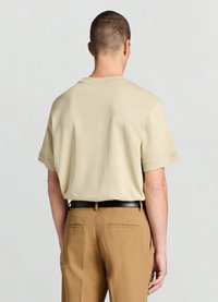 T-shirt en coton beige à manches courtes, col rond et coupe décontractée, associé à un pantalon marron et une ceinture noire.