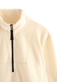 Krémově zbarvený fleecový pulovr s vysokým límcem a černým vertikálním předním zapínáním na půl zip.