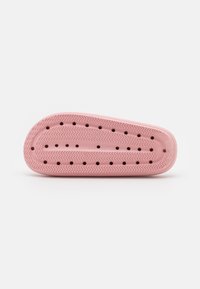 Suola di scarpa in gomma rosa con un motivo ondulato, dotata di molteplici fori di ventilazione e un bordo arrotondato per presa e flessibilità.