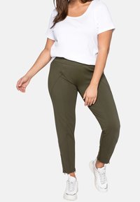Pantaloni verde oliva a sigaretta con cerniere alla caviglia, realizzati in tessuto morbido. Abbinati a una t-shirt bianca a girocollo e sneakers bianche.