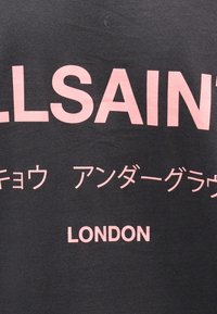 Μαύρο ύφασμα με μεγάλα ροζ γράμματα που σχηματίζουν το "LLSAINT", ιαπωνικούς χαρακτήρες από κάτω και τη λέξη "LONDON" σε μικρότερη ροζ γραφή στο κάτω μέρος.