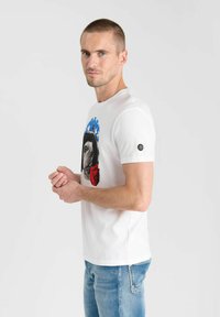 Camiseta de algodón blanca con un estampado gráfico de la cara de un perro con un diseño azul y rojo. Mangas cortas, cuello redondo y un acento de marca.