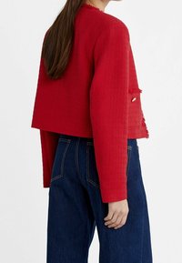 Rode geweven jas met een cropped ontwerp, rafelige randen en lange mouwen, gecombineerd met donkerblauwe high-waisted jeans.