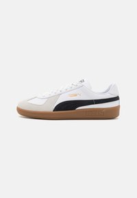 Zapatilla blanca con parte superior de ante y cuero, con un acento de ante negro, suela de goma color caramelo y logotipo dorado de Puma en el costado.