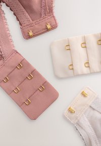 Estensioni per reggiseno in beige, rosa e bianco sporco con ganci metallici dorati, che mostrano diverse quantità di ganci e texture del tessuto su uno sfondo semplice.