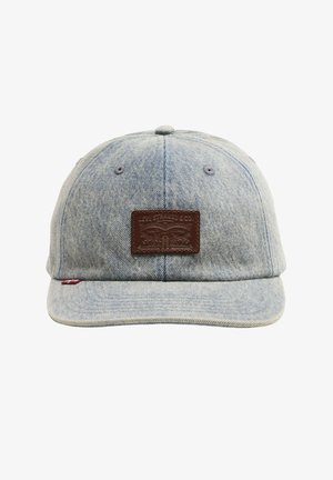 Gorra de béisbol de mezclilla azul claro con un parche de cuero marrón que presenta una marca en relieve en el frente.
