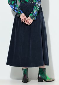 Marineblauwe corduroy rok met een geraffineerde tailleband, gecombineerd met multikleurige enkellaarsjes met groene en paarse accenten en een gestructureerd ontwerp.