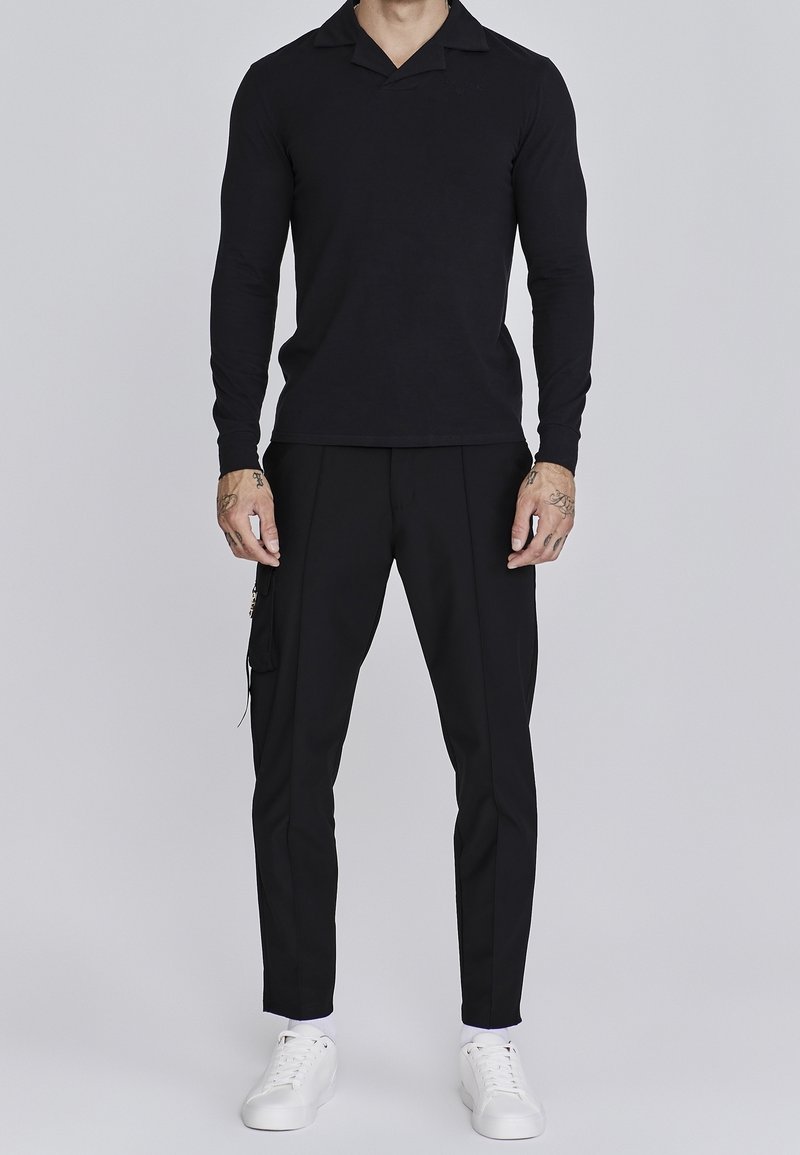 Zwart poloshirt met lange mouwen en een gestructureerde kraag, gecombineerd met zwarte op maat gemaakte broek en witte sneakers. Vloeiende stof en een aansluitend ontwerp.