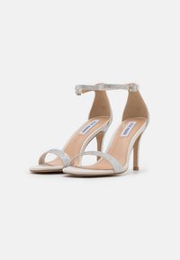 Sølv højhælede sandaler med et slankt design, der har rhinestones på ankelremmen og frontbåndene. Blød beige indersål.