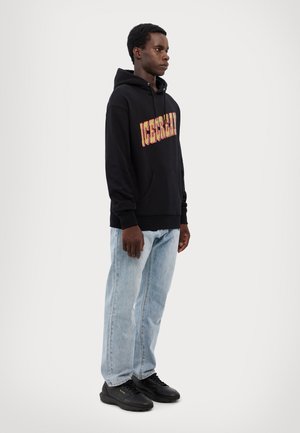 Black hoodie with "ICECREAM" in multicolored lettering, paired with light blue jeans and black athletic shoes. Simple design, casual fit.