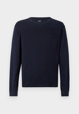 Tengerészeti hosszú ujjú póló pamutból, lekerekített nyakkivágással és egy kis mellzsebbel a bal oldalon. Simaság jellemzi.