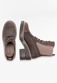 Botas marrones hasta el tobillo combinando cuero y tela, con punta redonda, cordones en la parte delantera y suela de goma texturizada. Presenta costuras en contraste y panel lateral.