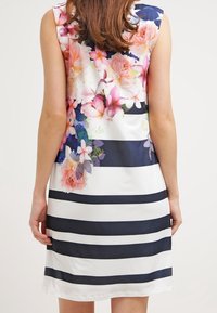 Mouwloze jurk met een bloemenpatroon in roze en paars op een gestreepte navy en witte achtergrond, met een gladde stoftextuur.