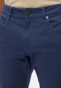 Granatowe bawełniane spodnie z zapięciem na guzik, kieszeniami z przodu i płaskimi szwami. Widoczna jest gładka tekstura oraz prosty krój nogawki.