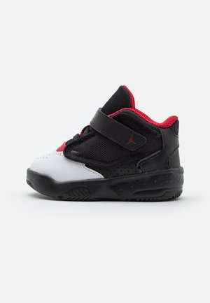 Chaussure de bébé noir, blanc et rouge avec une bride Velcro, semelle texturée et doublure intérieure rouge, vue de côté sur un fond uni.