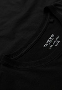 Musta t-paita pyöreällä kaula-aukolla, valmistettu 100 % puuvillasta. Erityispiirteinä sileä pinta ja huomaamaton brändilogo kauluksessa.