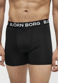 Buste masculin portant un boxer noir avec le logo Björn Borg sur la ceinture, debout devant un fond uni.