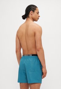 Ανδρικά σορτς κολύμβησης σε τιρκουάζ χρώμα με μαύρη ελαστική ζώνη που φέρει το λογότυπο "Calvin Klein". Περιλαμβάνει πίσω τσέπη, κατασκευασμένα από μαλακό, ελαφρύ υλικό.