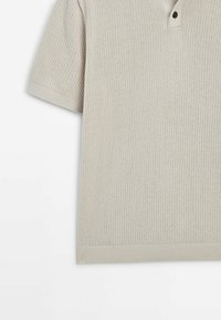 Beige lyhythihainen poolopaita, jossa on teksturoitu neuloskuvio, ja jossa on kolme nappia sisältävä listallinen aukko sekä resorireunat helmassa ja hihansuissa.