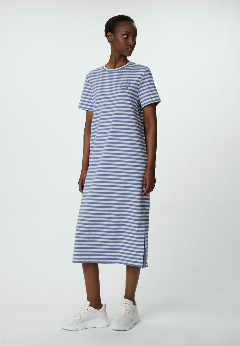 Gestreiftes Maxikleid aus blauem und weißem Baumwollstoff, mit kurzen Ärmeln, Rundhalsausschnitt und Seitenschlitzen, kombiniert mit weißen Sneakers.