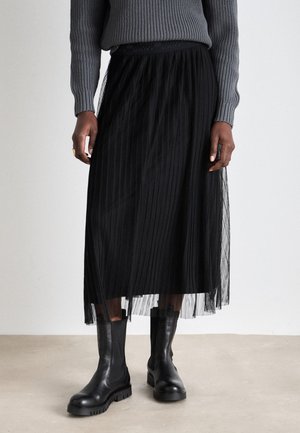 Schwarzer, plissierter Midirock aus Tüll mit elastischem Bund. Kombiniert mit schwarzen Knöchelstiefeln und einem grauen Strickpullover.