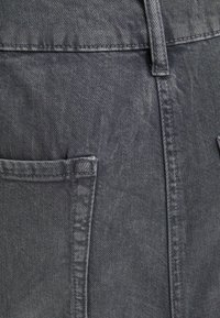 Tela de denim gris con una superficie ligeramente texturizada, con costuras visibles y un bolsillo lateral. El diseño incluye una cintura alta.