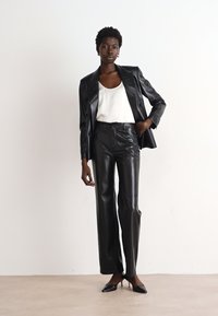 Black faux leather blazer and matching pants, tailored fit, smooth texture, paired with a white satin tank top and black heels.