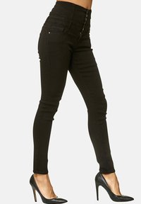 Schwarze, hochtaillierte Skinny-Jeans aus Denim, mit einem Fünf-Knopf-Verschluss, figurbetonten Beinen und minimalistischem Design. Kombiniert mit schwarzen High Heels.