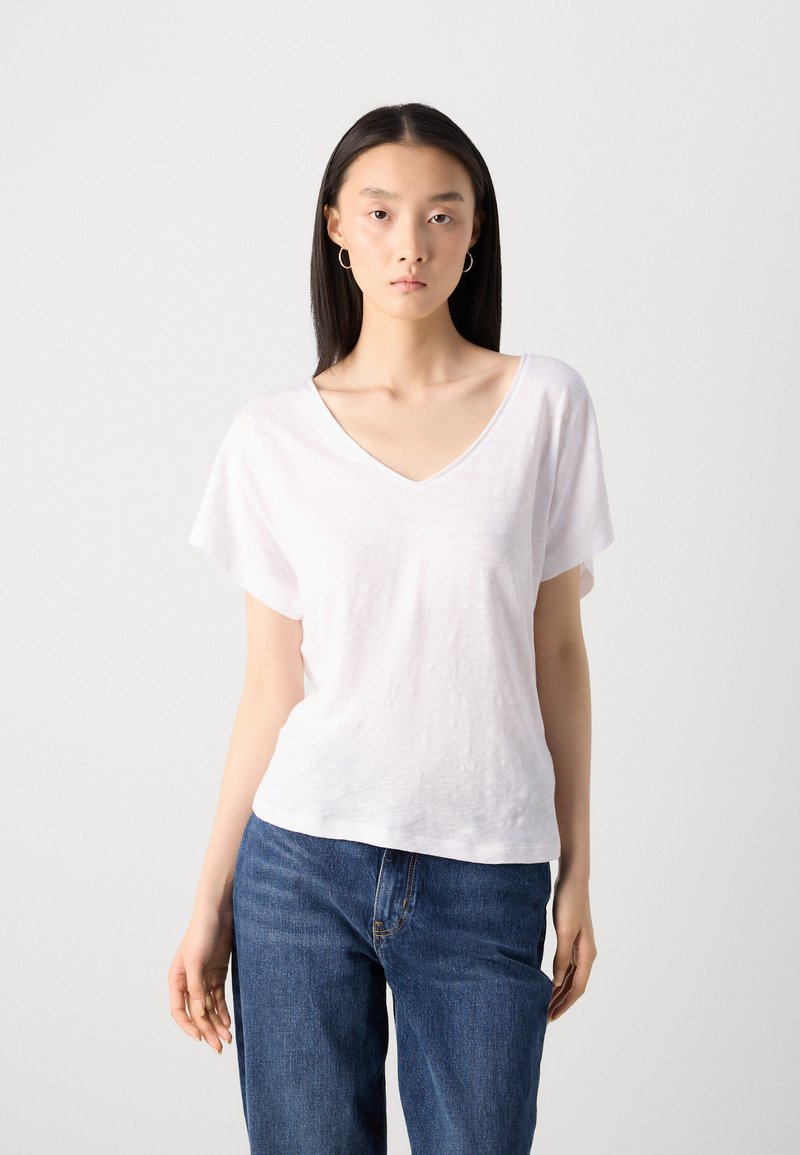 Biała koszulka polo z krótkim rękawem, wykonana z lekkiego materiału, połączona z niebieskimi dżinsami. Prosty design z minimalnymi detalami tekstur.