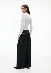 Maglietta bianca a maniche lunghe abbinata a jeans scuri a vita alta e gamba ampia, con grandi tasche posteriori e dettagli di cucitura a contrasto.