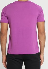 Tričko s krátkým rukávem v jednobarevné fialové, vyrobené z elastické látky. Má zaoblený výstřih a ploché švy, s volným střihem.