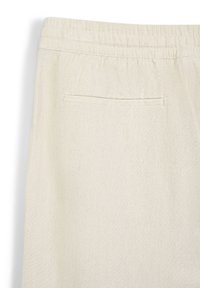 Tessuto beige chiaro con vita elasticizzata e una tasca a welt orizzontale sul retro, che mostra un materiale morbido e testurizzato.